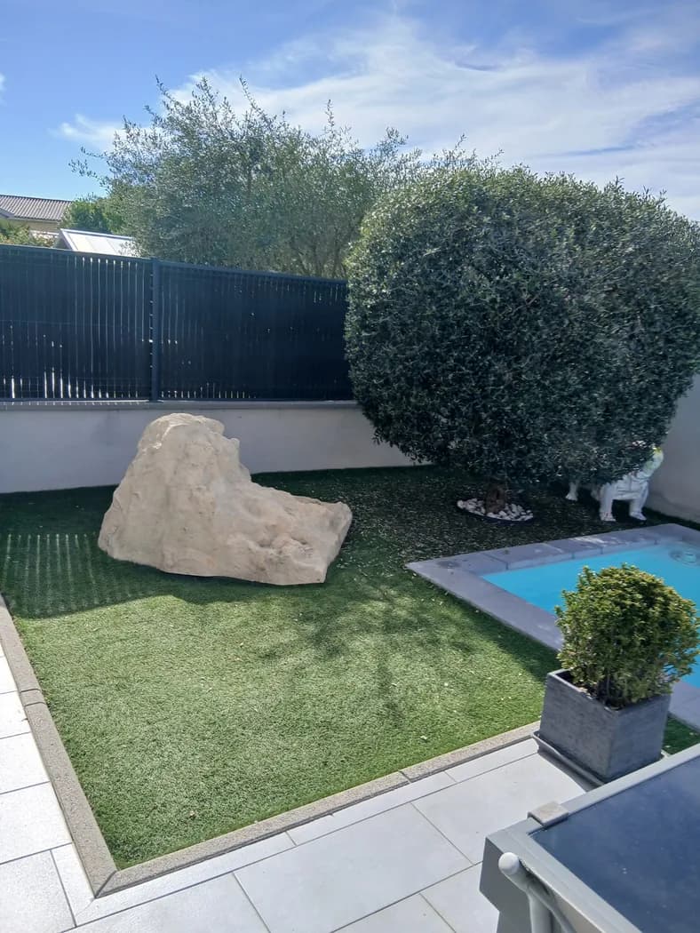 Gazon synthétique posé autour d’une piscine, avec un rocher et un olivier